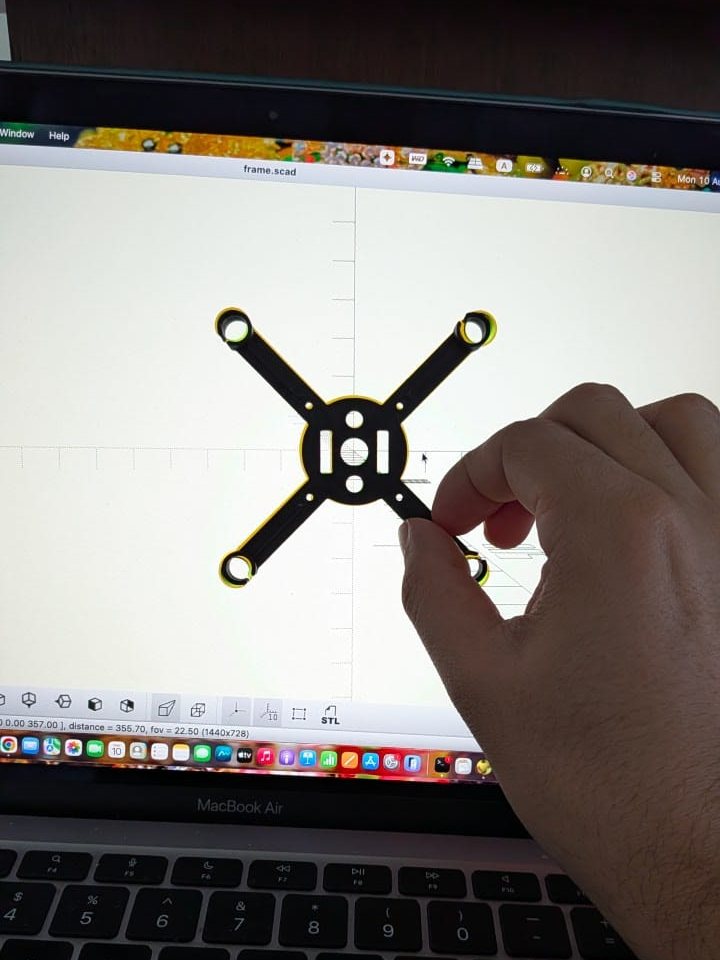 The printed black frame held up in front of a laptop that shows the same frame in OpenSCAD