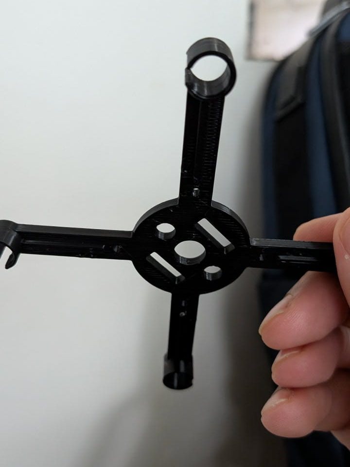 The printed frame at an angle, showing the motor rings at the ends of the arms and the strap slots in the centre plate